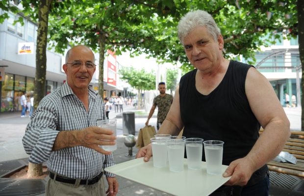 Ingo Wilke (rechts) verteilt an heißen Tagen Wasser in der Bahnhofstraße. Wer durstig ist, wie Bakri Nabin, bekommt einen Becher. Foto: Becker & Bredel.