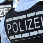 In Polizei-Westen gekleidete Polizisten stehen mit dem Rücken zur Kamera. Foto: Silas Stein/Archivbild