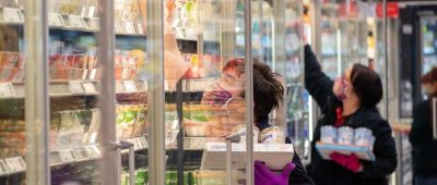 Mitarbeiterinnen in einem Supermarkt tragen Schutzmasken, während sie die Kühlregale mit Waren bestücken. Foto: Robert Michael/dpa-Zentralbild/dpa